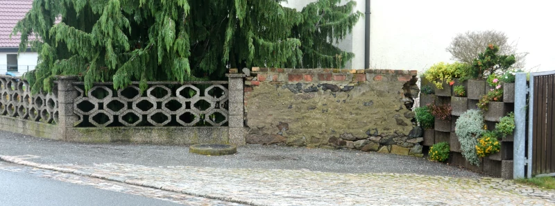 Drei Epochen der Umfriedung - links DDR-Betonelemente-Zaun, Mitte Bruchsteinmauer, Rechts Beton-Pflanzkübel BRD