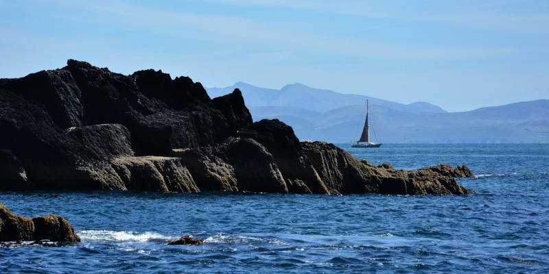 Ireland: Sailing boat between the coastal cliffs of Dingle peninsula